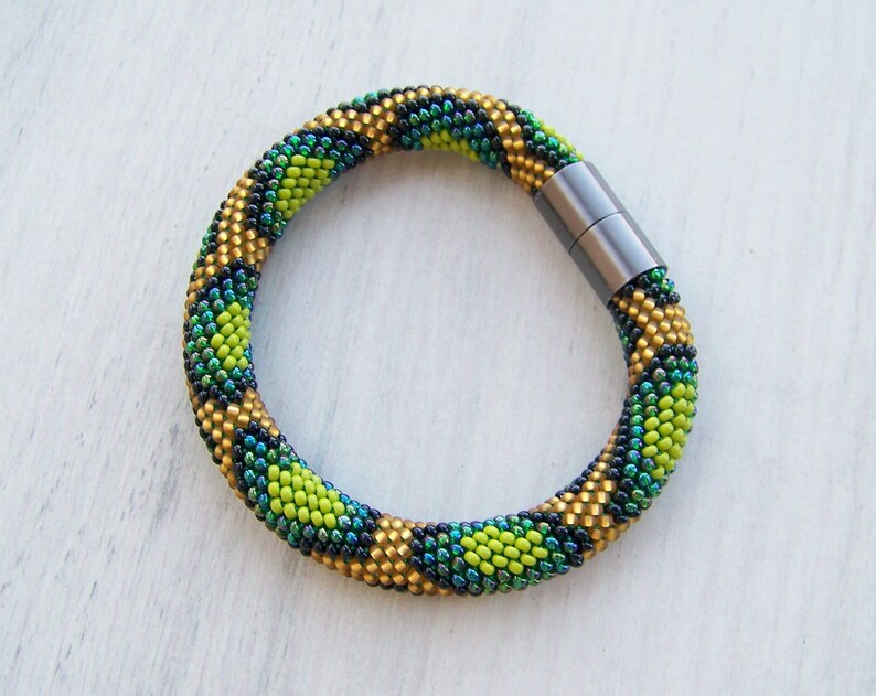 May include: A green, gold, and black beaded bracelet with a magnetic clasp.