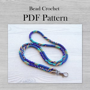 May include: A beaded lanyard with a blue, turquoise, and gold color scheme. The lanyard has a silver clasp and is shown on a white wooden surface. Bead Crochet PDF Pattern.