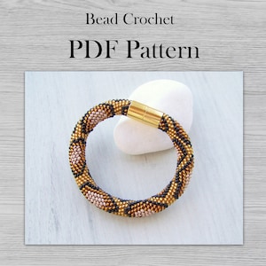 Könnte beinhalten: Ein Armband aus Perlen mit einem Leopardenmuster in Schwarz, Gold und Rosa. Das Armband hat einen Magnetverschluss und wird auf einem weißen Stein gezeigt.