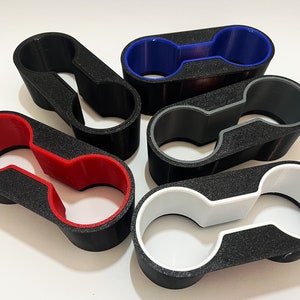 Könnte beinhalten: Fünf verschiedene farbige Getränkehalter. Die Getränkehalter sind aus schwarzem Kunststoff mit einem farbigen Innenring. Die Farben sind Rot, Blau, Grau und Weiß.