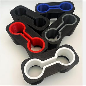 Puede incluir: Un conjunto de cinco portavasos de espuma negra con anillos interiores de diferentes colores. Los anillos son rojo, azul, blanco y gris.