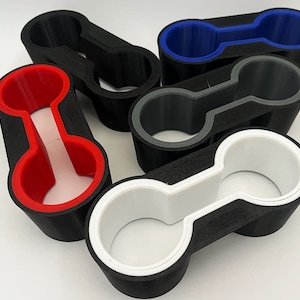 Könnte beinhalten: Fünf schwarze Getränkehalter mit unterschiedlich farbigen Innenräumen. Die Getränkehalter sind so konzipiert, dass sie verschiedene Getränkegrößen aufnehmen können. Die Farben der Innenräume sind rot, blau, weiß und grau.