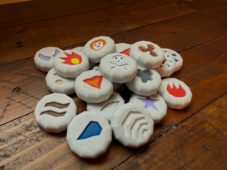 Puede incluir: Una colecci&oacute;n de fichas de juego redondas y blancas con varios s&iacute;mbolos y colores. Los s&iacute;mbolos incluyen una calavera y huesos cruzados, una llama, una estrella, una ola y una luna creciente. Las fichas est&aacute;n hechas de un material texturizado y tienen un borde ligeramente elevado.