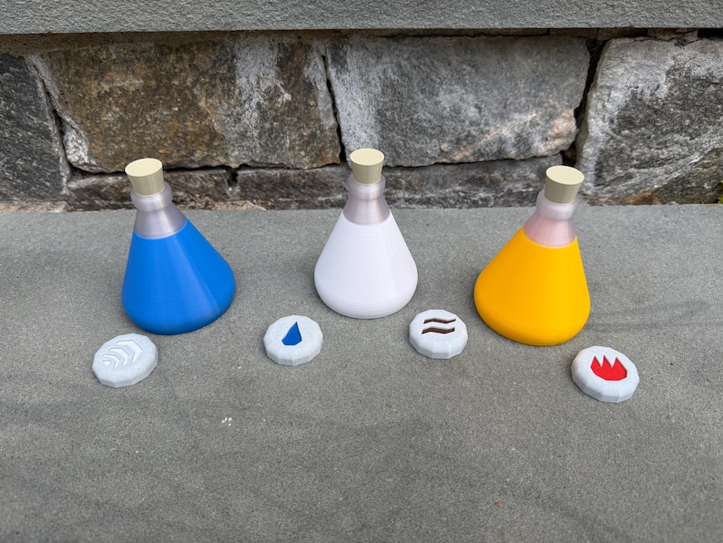 May include: Three colorful potion bottles with matching elemental symbols. The bottles are blue, white, and yellow, each with a light tan stopper. The symbols are water, earth, and fire.