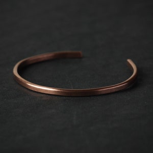 Può includere: Un semplice braccialetto in rame con una finitura liscia e lucida.