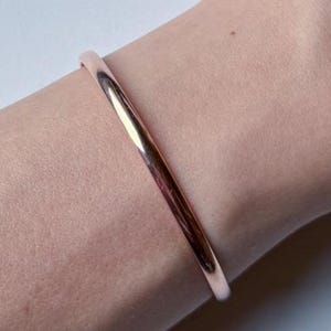 May include: A simple rose gold bangle bracelet on a person's wrist.