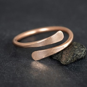 Op de afbeelding: Een eenvoudige, minimalistische roségouden ring met een uniek, gedraaid ontwerp. De ring is gemaakt van één stuk metaal dat gebogen en gedraaid is om een unieke vorm te creëren.