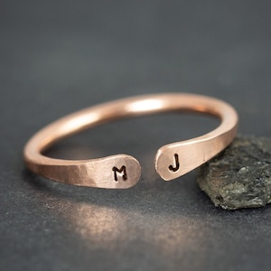 May include: A copper ring with a split design, featuring the initials "M" and "J" engraved on each side.