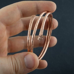 Peut inclure: Ensemble de trois bracelets en spirale de couleur cuivre, finition martelée. Les bracelets sont présentés sur fond sombre. La texture martelée donne aux bracelets un aspect unique et artisanal. Design simple et élégant.