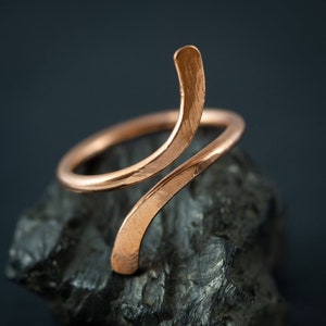 May include: A copper ring with a unique, curved design. The ring is made from a single piece of wire that is twisted and shaped into a spiral.