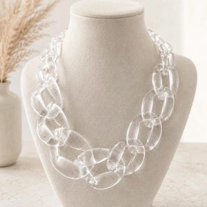 Puede incluir: Un collar de cadena transparente y grueso, exhibido en un maniquí. El collar está hecho de eslabones grandes y ovalados. El material transparente le da al collar un aspecto moderno y audaz. Una pieza llamativa.