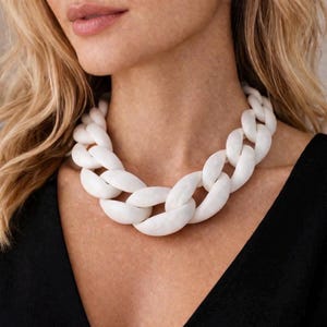 May include: A chunky white chain necklace. The necklace is made of large, oval-shaped links. The necklace is worn around the neck, and the background is blurred.