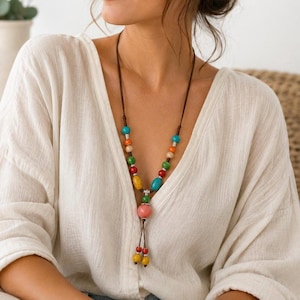 Peut inclure: Un long collier composé d'un cordon marron foncé orné de perles en bois multicolores dans des tons turquoise, orange, jaune, vert et rose, agrémenté de petites entretoises en métal argenté et de deux perles pendantes à l'extrémité inférieure.