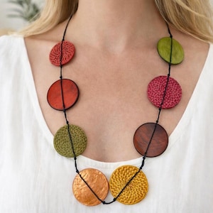 Può includere: Una collana multicolore con pendenti circolari rossi, verdi, arancioni e gialli. La collana è infilata su un cordino nero e presenta trame intrecciate e lisce. Un accessorio di moda.