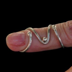 May include: A silver ring with a wavy design and small beads. The ring is worn on a finger.