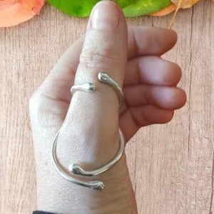 May include: A silver thumb ring with a unique, twisted design. The ring is made of a single piece of metal that is bent and twisted to create a unique shape.