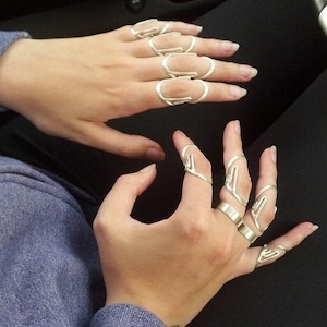 May include: A pair of hands wearing multiple silver rings made from bent wire. The rings are worn on multiple fingers on each hand.