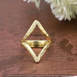 Può includere: Un anello color oro con un design geometrico a forma di diamante. L'anello è realizzato in metallo martellato e ha una finitura testurizzata.