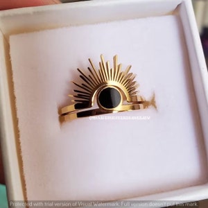 May include: Gold ring with a black sun design. The ring is made of two bands, one with a sunburst design and the other with a black circle in the center.