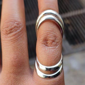 Pode incluir: Um conjunto de três anéis de prata usados em um dedo. Os anéis são empilhados um em cima do outro e são feitos de um metal liso e brilhante.