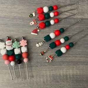 Peut inclure: Quatre ensembles de bijoux en perles et fil sur le thème de Noël. Chaque ensemble présente un charme différent, notamment un bonhomme de neige, un flocon de neige, un sapin de Noël et une couronne. Les perles sont rouges, vertes et blanches.