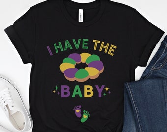 May include: Black t-shirt with a green, purple, and gold donut design and the text "I have the baby".
