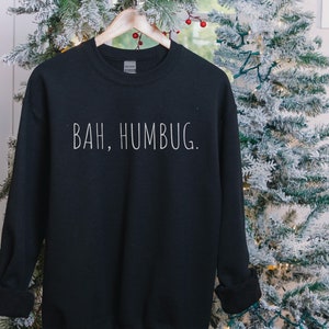 May include: Black sweatshirt with white text that reads "BAH, HUMBUG." The sweatshirt is hanging on a hanger in front of a Christmas tree.
