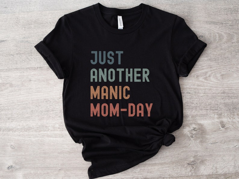May include: Black t-shirt with the text "Just Another Manic Mom-Day" in a vintage style font with colourful letters.