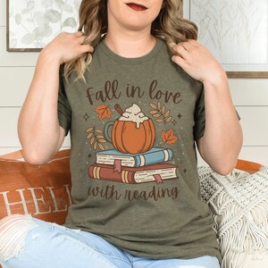 Pode incluir: Uma camiseta verde com o texto "Fall in love with reading" e um gr&aacute;fico de um latte de ab&oacute;bora em cima de uma pilha de livros.