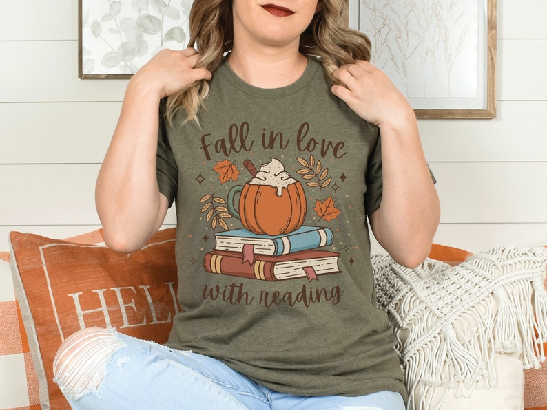 Pode incluir: Uma camiseta verde com o texto "Fall in love with reading" e um gr&aacute;fico de um latte de ab&oacute;bora em cima de uma pilha de livros.