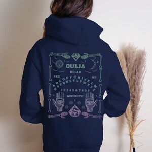 May include: Navy blue hoodie with a Ouija board design on the back. The design includes a skeleton frame, sun, moon, hands, and the words "OUJA", "HELLO", "YES", "NO", and "GOODBYE". The design is in shades of green and purple.