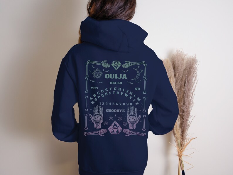 May include: Navy blue hoodie with a Ouija board design on the back. The design includes a skeleton frame, sun, moon, hands, and the words "OUJA", "HELLO", "YES", "NO", and "GOODBYE". The design is in shades of green and purple.