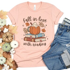 Pode incluir: Uma camiseta cor de p&ecirc;ssego com o texto "Apaixone-se pela leitura" e um gr&aacute;fico de um latte de especiarias de ab&oacute;bora em cima de uma pilha de livros.