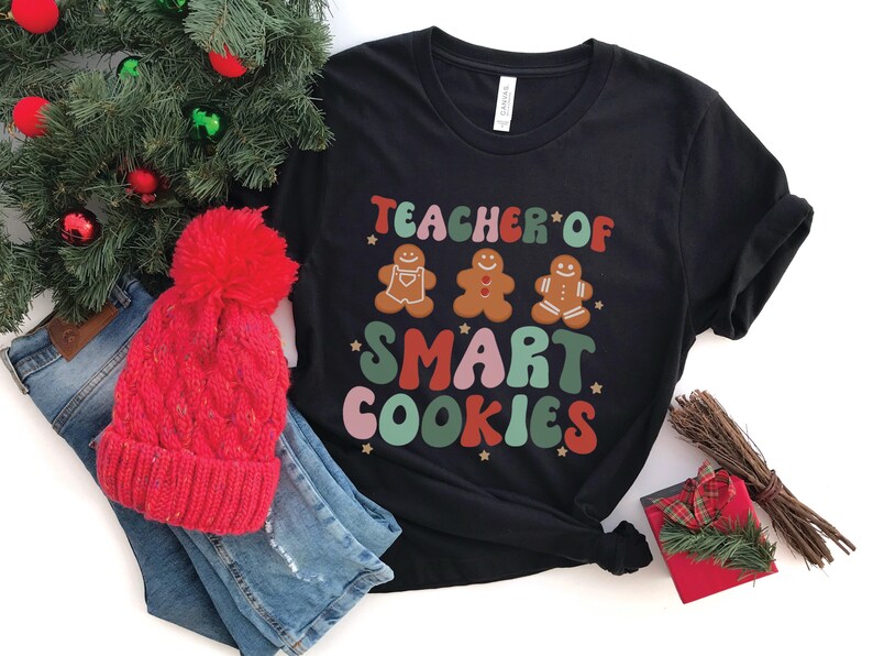 May include: Black t-shirt with the text "Teacher of Smart Cookies" in colorful letters. Three gingerbread cookies are depicted above the text.