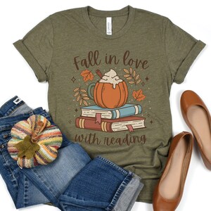 Pode incluir: Uma camiseta verde com o texto "Fall in love with reading" e uma imagem de desenho animado de um latte de especiarias de ab&oacute;bora com chantilly em cima de uma pilha de livros.