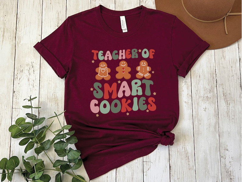 May include: Burgundy t-shirt with a graphic design that says "Teacher of Smart Cookies" with gingerbread men illustrations.