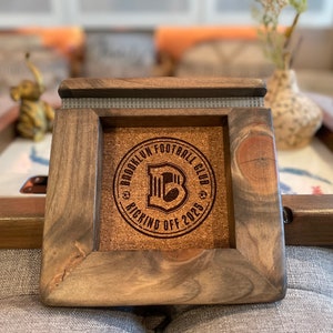 May include: A wooden coaster with a cork inlay featuring a logo that says "Brooklyn Football Club Kicking Off 2025".