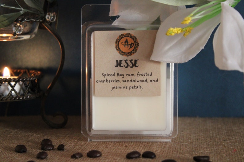 May include: A white wax melt in a clear plastic container with a brown label that reads "Jesse Spiced Bay rum, frosted cranberries, sandalwood, and jasmine petals."