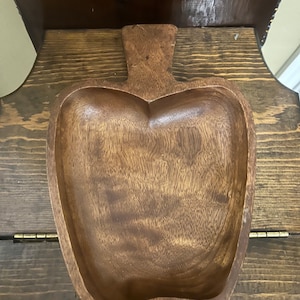 May include: A dark brown wooden bowl shaped like an apple. The bowl has a smooth, polished finish and a slightly rounded bottom.