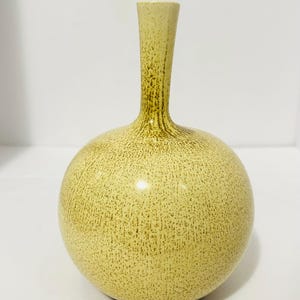 May include: A decorative, spherical vase with a narrow neck. The vase has a speckled, light-yellow finish with brown accents. The vase is a decorative item for the home.