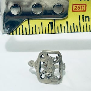May include: A silver-toned metal ring featuring a cutout design of a cartoon mouse character. The ring is positioned below a yellow measuring tape, which indicates the ring's height is approximately 0.5 inches from the top to the bottom edge.