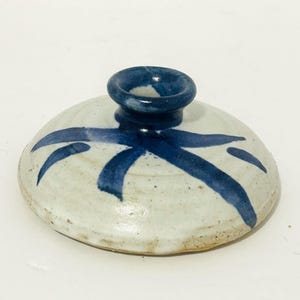 May include: A small white ceramic vase with a blue glaze and a blue abstract design. The vase has a round base and a narrow neck.