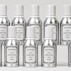 May include: Ten silver-colored metal bottles with white caps, arranged in two rows. Each bottle features a rectangular white label with a black decorative border, the text ASLI ATTAR, the words SAMPLE PACK, and the volume measurement 25 ML.