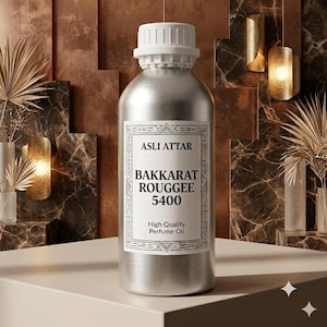 May include: A silver-colored metal bottle with a white screw-top cap. The label features the text ASLI ATTAR, BAKKARAT ROUGGEE 5400, and High Quality Perfume Oil, framed by a decorative border with geometric patterns and small symbols.