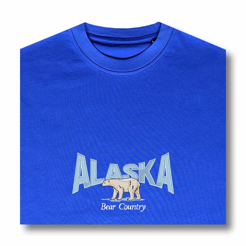 May include: A royal blue t-shirt with a white polar bear and the text "ALASKA Bear Country" in a white, blue, and gray font.