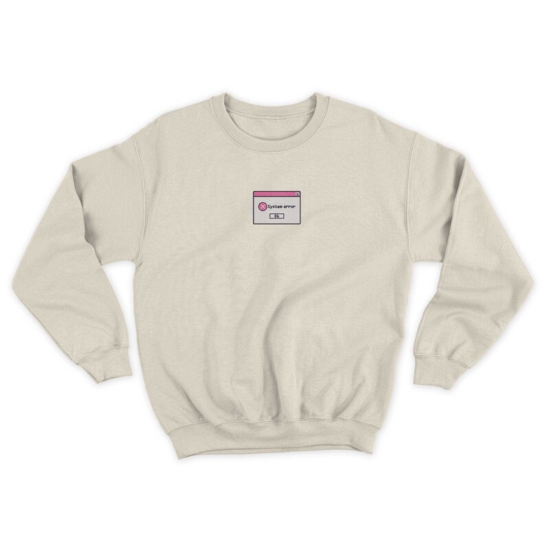 May include: A light beige sweatshirt with a small embroidered design of a pink and white computer error message. The message reads "System error".