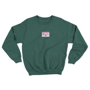 May include: A dark green sweatshirt with a small embroidered image of a computer error message. The message reads "System error" and is in a white box with a pink border.
