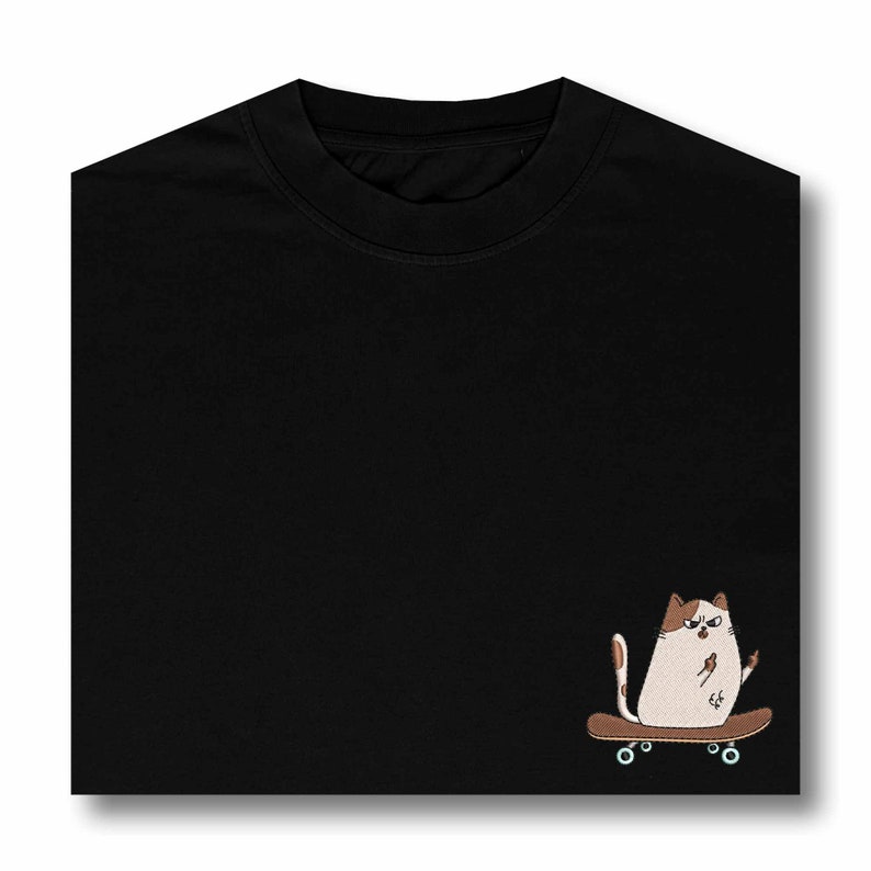 Op de afbeelding: Zwart T-shirt met een witte kat die skateboardt. De kat is bruin en wit en heeft een chagrijnige uitdrukking.