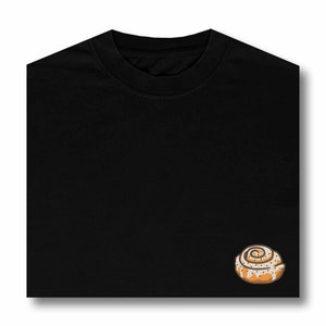 May include: Black t-shirt with a cinnamon roll embroidered on the right side of the chest.