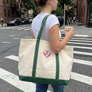 Canvas tote bag featuring a red and white skeleton couple heart embroidery, carried as part of a casual city outfit.